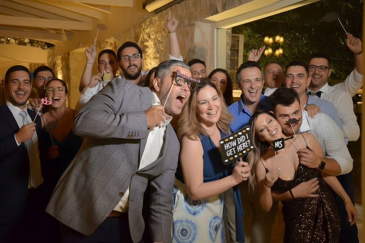 Group of people posing indoors at a party, holding photo booth props and smiling at the camera.